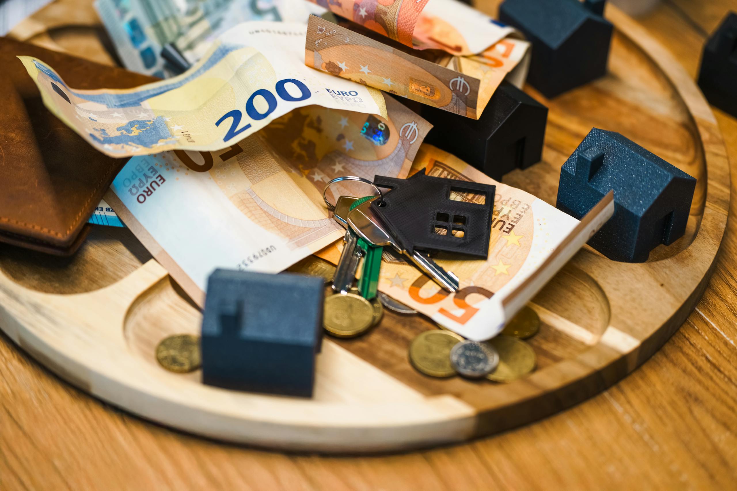 Euro currency, keys, and miniature houses symbolize real estate and finance concepts.
